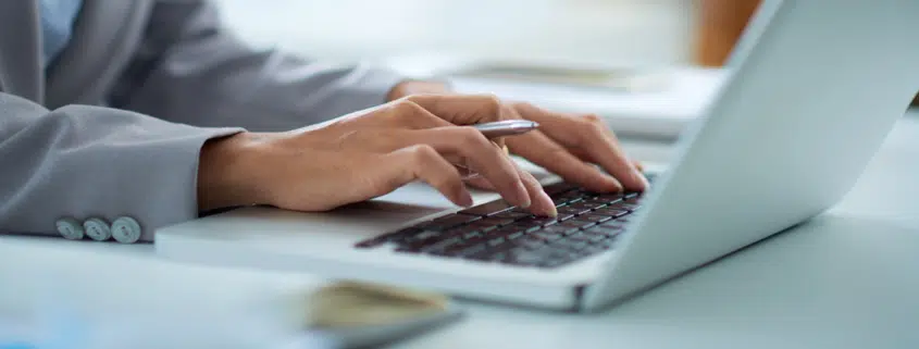 hands typing on a computer while reviewing owned media